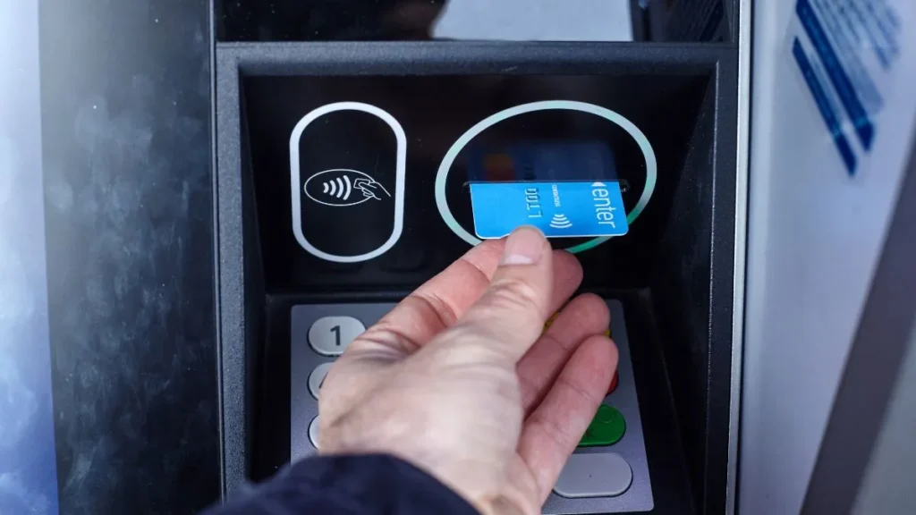 Mano sosteniendo una tarjeta de débito frente a un cajero automático